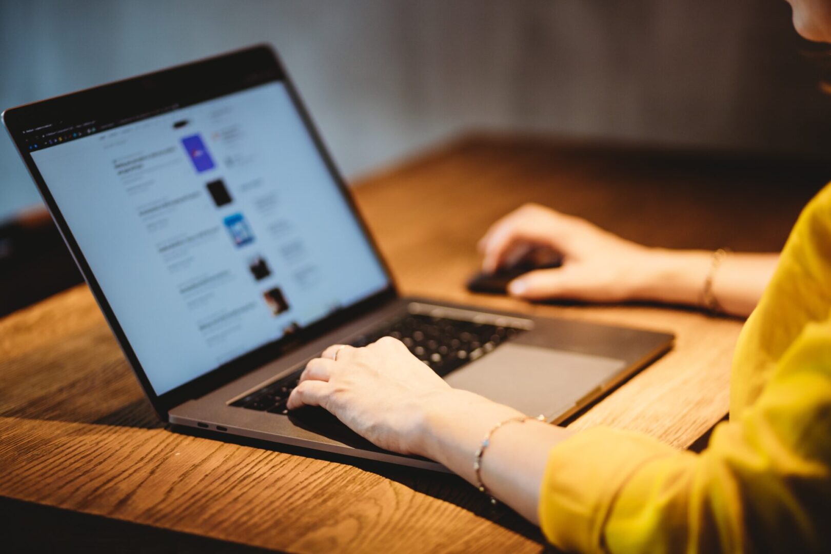 A person using a laptop on top of a wooden table.