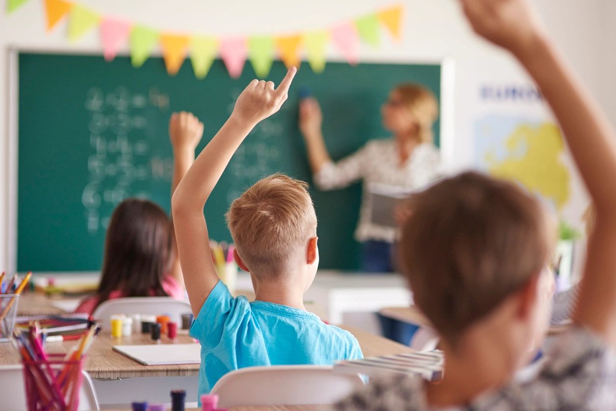 Students raising hands in a classroom setting.